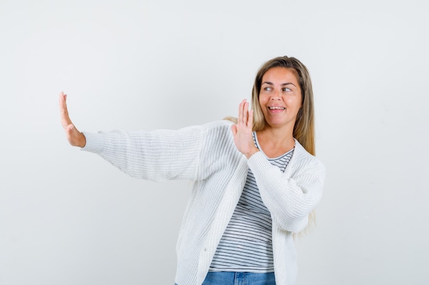 Молодая женщина показывает жест остановки в футболке, куртке и выглядит счастливым, вид спереди.