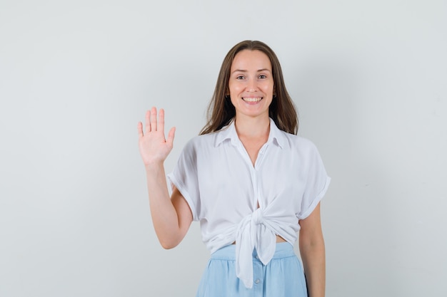 Young woman showing stop sign in white blouse and light blue skirt and looking cheerful