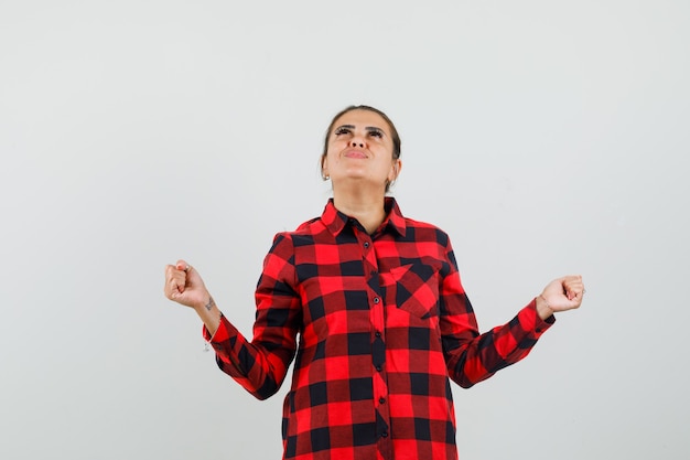 Foto gratuita giovane donna che mostra il gesto di successo in camicia a quadri e guardando grato, vista frontale.