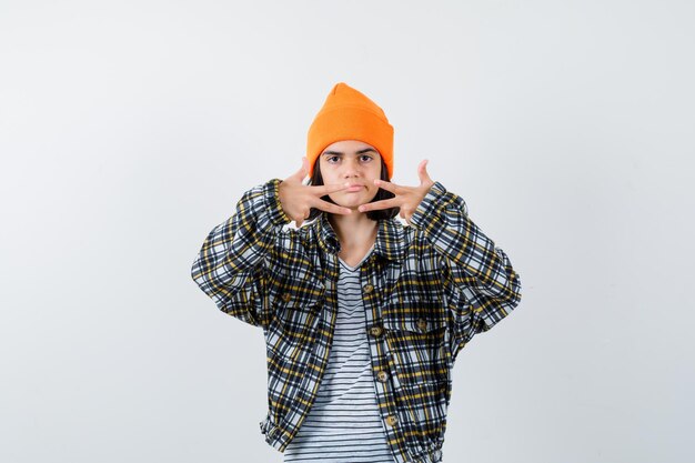 Young woman showing three fingers in orange hat and checkered shirt and looking unhappy
