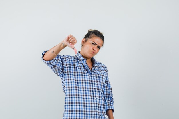 Young woman showing thumb down in checkered shirt and looking upset.