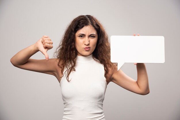 Young woman showing a thumb down and holding blank white poster. High quality photo