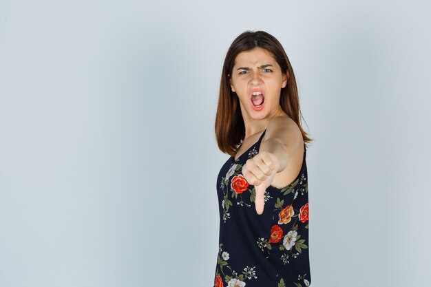 Young woman showing thumb down while screaming in blouse and looking aggressive.