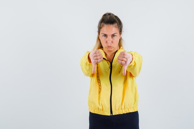 Young woman showing thumb down in yellow raincoat and looking displeased
