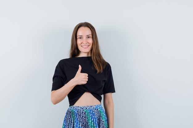 Young woman showing thumb up in black t-shirt and blue skirt and looking attractive