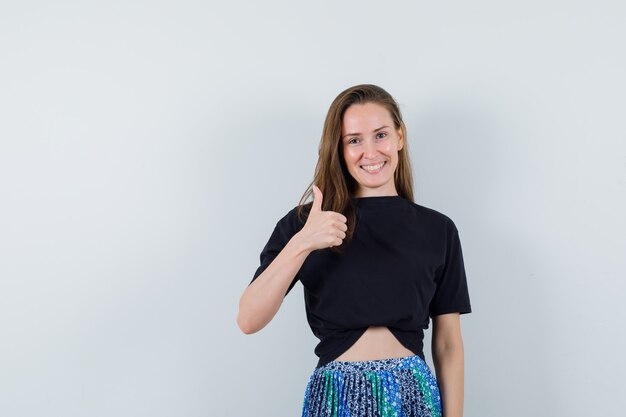 Young woman showing thumb up in black t-shirt and blue skirt and looking happy