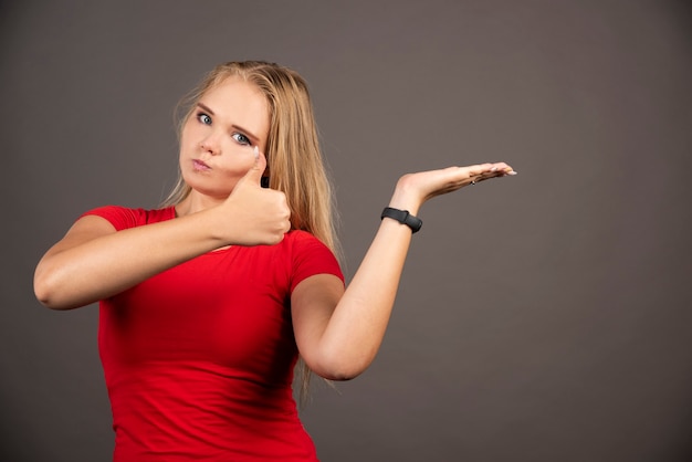 Young woman showing thumb up on black wall.