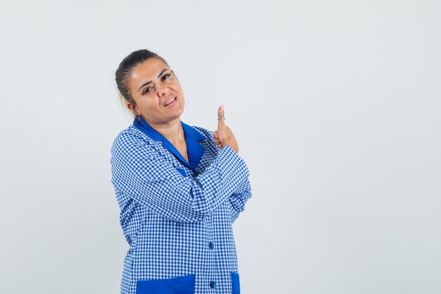 Young woman showing thumb up in blue gingham pajama shirt and looking pretty , front view.