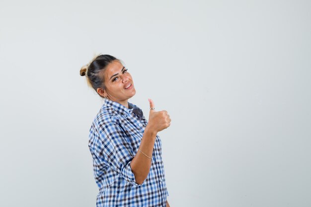 Young woman showing thumb up in checkered shirt.