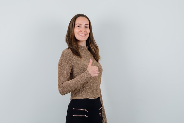 Young woman showing thumb up in gold gilded sweater and black pants and looking happy