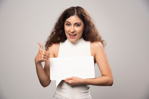 Young woman showing a thumb up and holding blank white poster. High quality photo