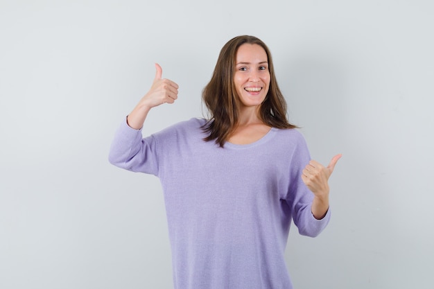 Young woman showing thumb up in lilac blouse and looking optimistic 