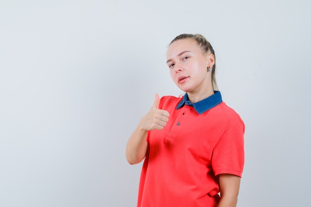 Young woman showing thumb up in t-shirt and looking confident