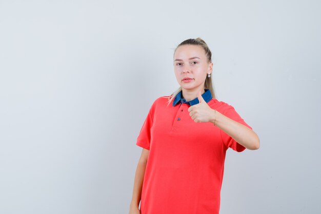 Молодая женщина показывает палец вверх в футболке и выглядит уверенно