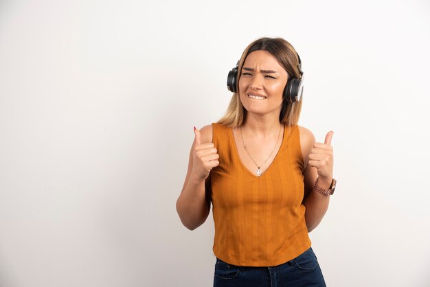 Young woman showing thumb up and wearing headphones over white background.