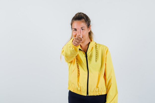 Young woman showing thumb up in yellow raincoat and looking glad