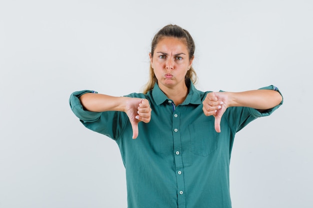 Free photo young woman showing thumbs down and puffing cheeks in green blouse and looking displeased