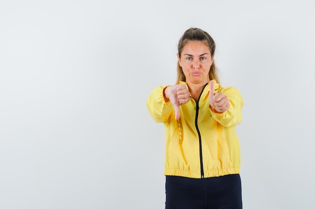 Free photo young woman showing thumbs down with both hands in yellow bomber jacket and black pants and looking cute