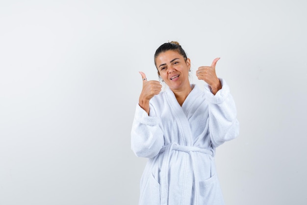 Young woman showing thumbs up in bathrobe and looking confident