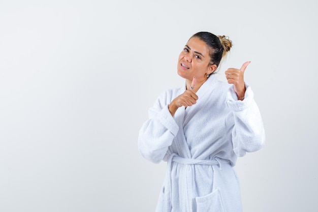 Young woman showing thumbs up in bathrobe and looking confident