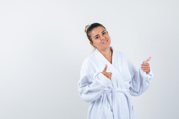 Young woman showing thumbs up in bathrobe and looking confident