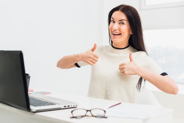 Free photo young woman showing thumbs up sitting at table