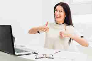 Free photo young woman showing thumbs up sitting at table