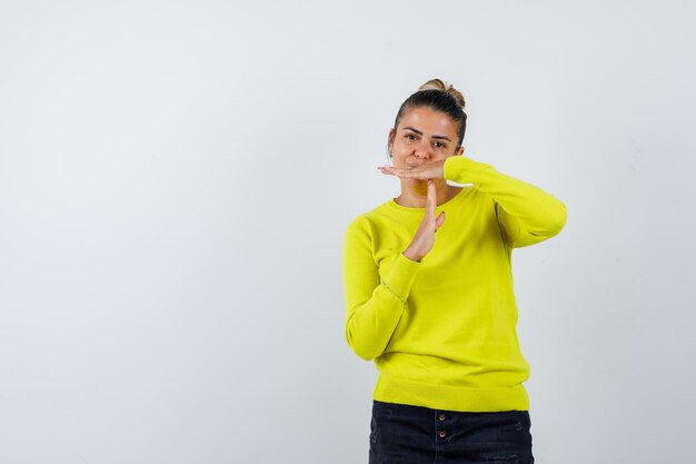 Young woman showing time-break gesture in yellow sweater and black pants and looking serious