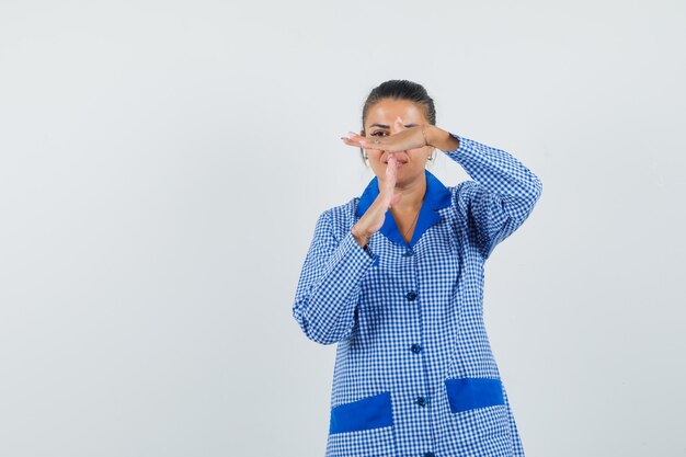 Young woman showing time-break pose in blue gingham pajama shirt and looking pretty. front view.