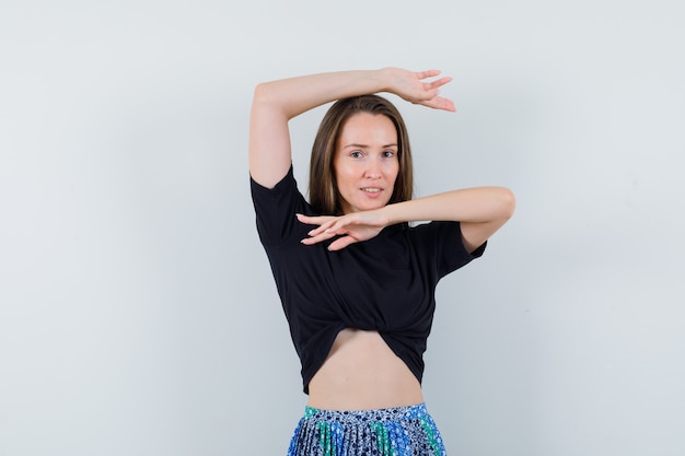 Free photo young woman showing traditional dance gesture in black t-shirt and blue skirt and looking happy