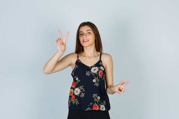 Young woman showing V-sign in floral top and looking peaceful