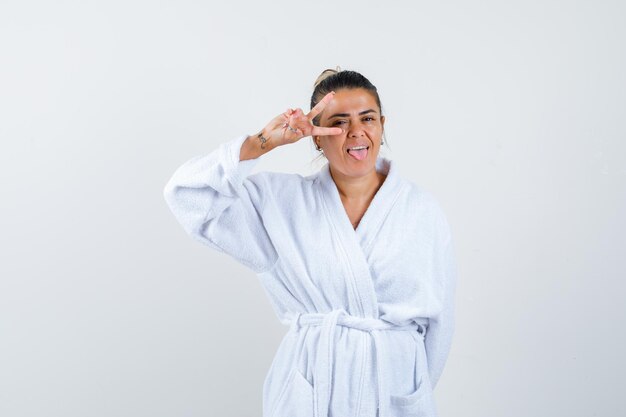 Young woman showing victory gesture in bathrobe and looking lucky