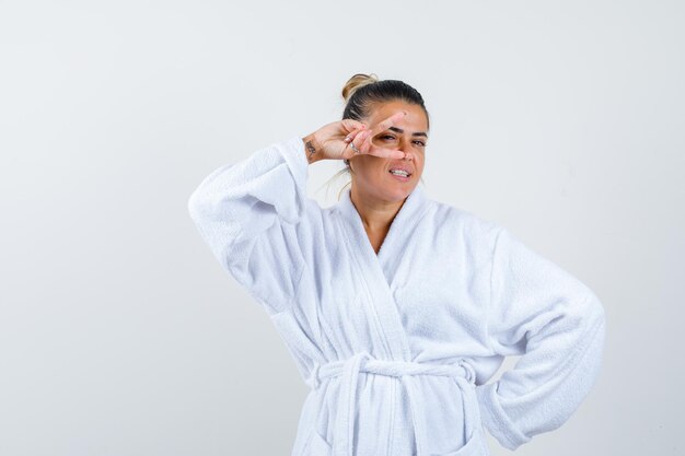 Young woman showing victory sign in bathrobe and looking lucky