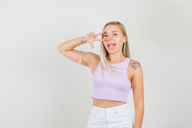 Young woman showing victory sign near eye in singlet