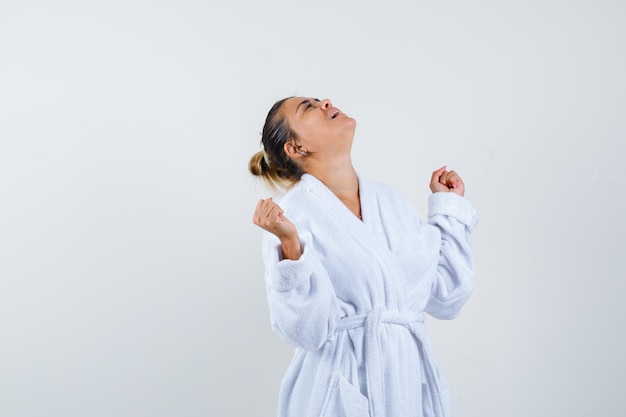 Free photo young woman showing winner gesture in bathrobe and looking lucky
