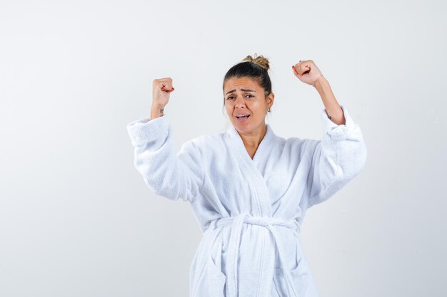 Young woman showing winner gesture in bathrobe and looking lucky