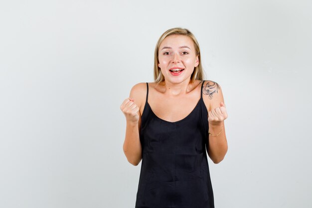 Young woman showing winner gesture in black singlet and looking happy