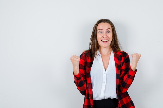 Young woman showing winner gesture in casual clothes and looking happy. front view.