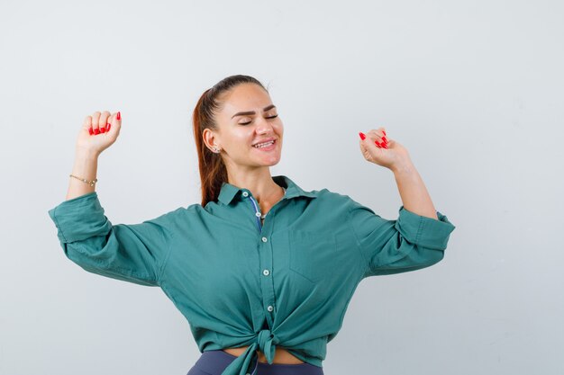 緑のシャツで勝者のジェスチャーを示し、幸運に見える若い女性。正面図。