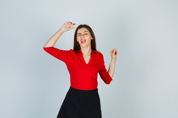 Young woman showing winner gesture in red blouse, black skirt and looking lucky