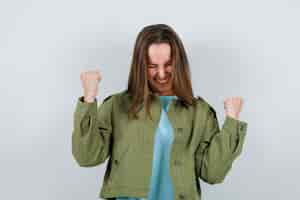 Free photo young woman showing winner gesture in t-shirt, jacket and looking lucky , front view.