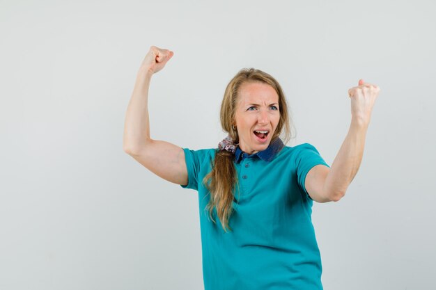 Tシャツで勝者のジェスチャーを示すと幸せそうに見えて若い女性