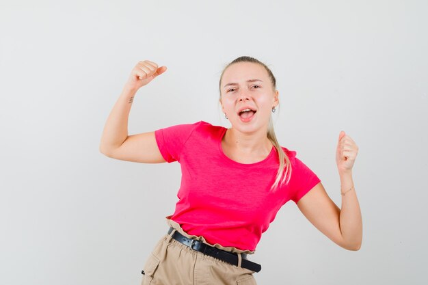 Tシャツとズボンで勝者のジェスチャーを示し、幸せそうに見える若い女性