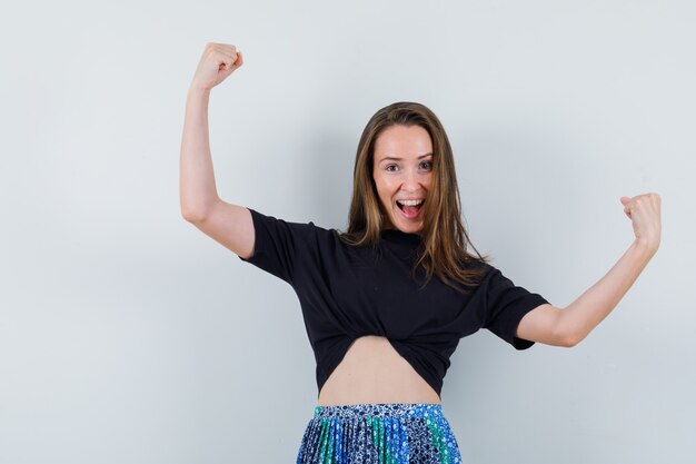 Young woman showing winner pose in black t-shirt and blue skirt and looking happy