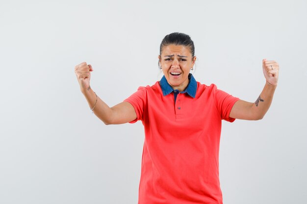 Young woman showing winner pose in red t-shirt and looking pretty , front view.