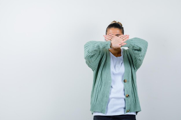 Young woman showing x gesture in white t-shirt and mint green cardigan and looking serious