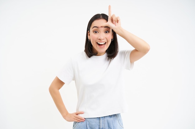 Free photo young woman shows l letter loser gesture on forehead mocking someone makes fun of person standing ov