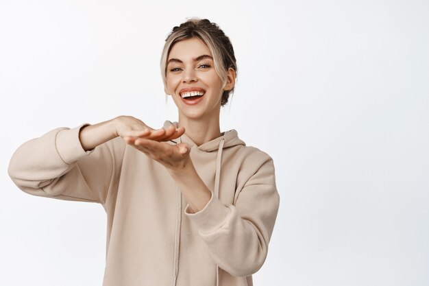 Young woman shows spending trowing money gesture and smiling, concept of business and earning cash, standing on white