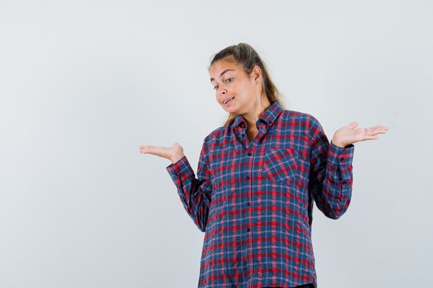 Young woman shrugging shoulders in checked shirt and looking perplexed