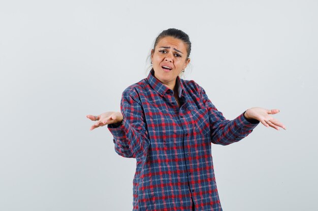 Free photo young woman shrugging shoulders in checked shirt and looking pretty , front view.